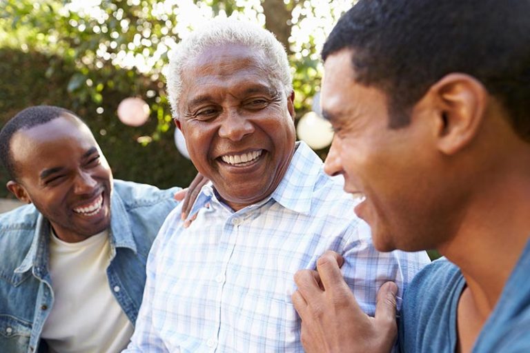 An older man laughing with his two adult sons outdoors
